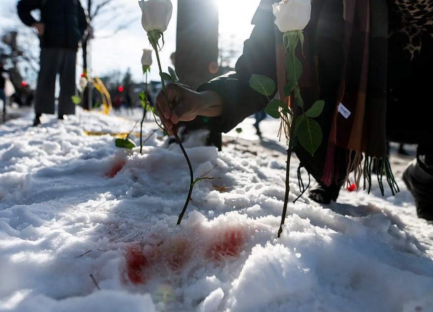 People placing flowers in the snow near the scene of the shooting